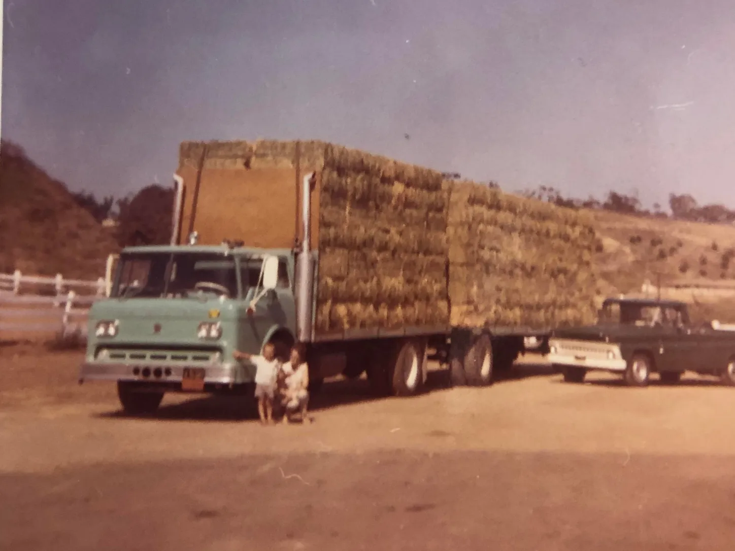 Historic farm truck hauling stacked hay bales through a rural setting.
